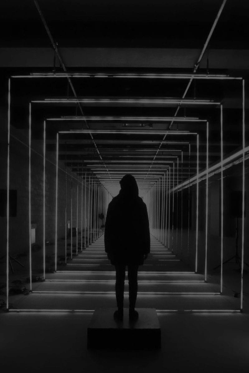 A lone person stands in front of an art installation in black and white